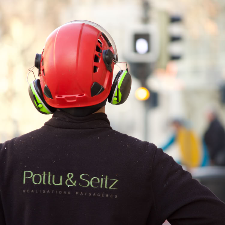 Rond-point à Meinier avec des arbres et des fleurs au centre, entouré d'une route, ciel partiellement nuageux.