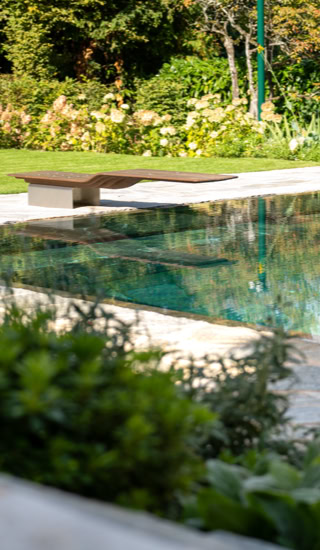 Piscine extérieure entourée de verdure et de fleurs, avec un banc en bois à côté.