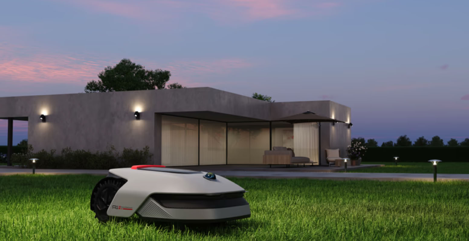 Tondeuse robotique Dreame sur une pelouse verte devant une maison moderne au crépuscule.