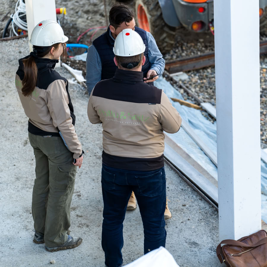 2 architectes paysagistes et un technicien portant des casques de sécurité discutent sur un chantier.