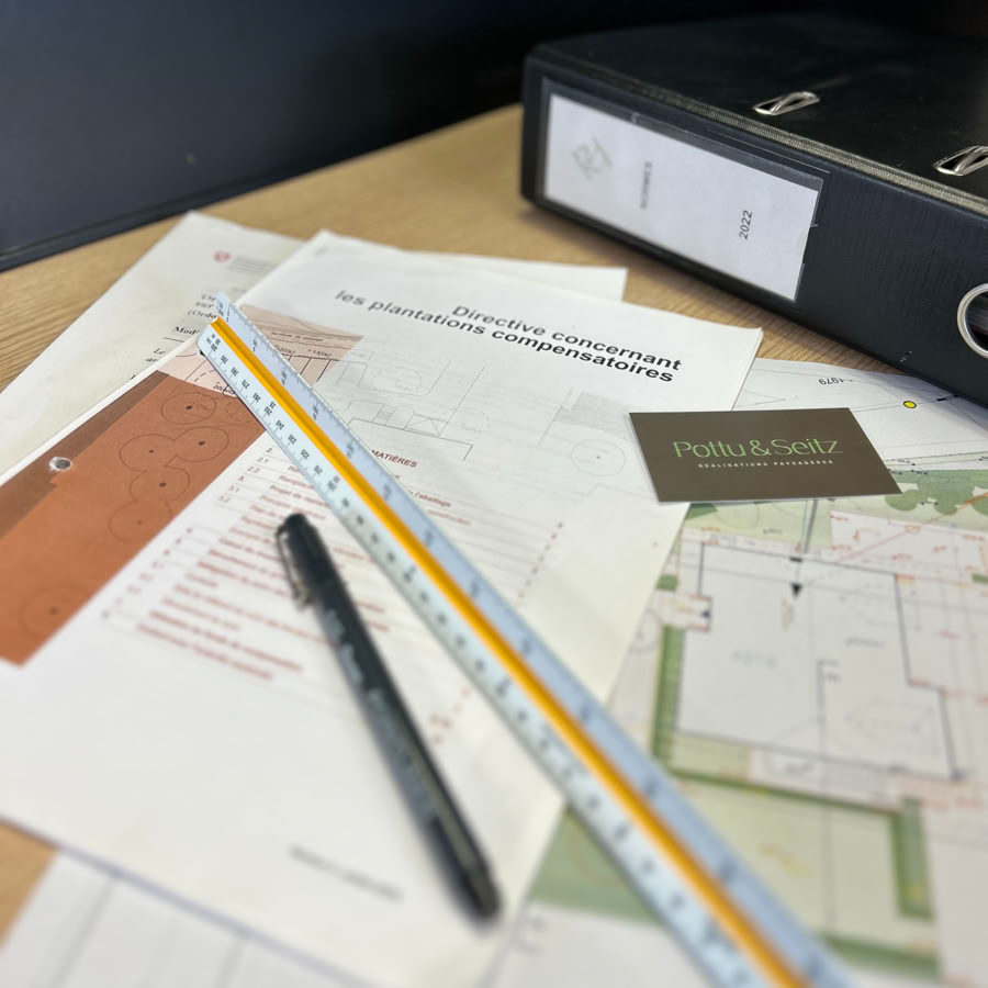 Documents et plans sur une table avec un stylo, une règle et un classeur noir chez Pottu & Seitz, architecte paysagiste à Genève et Vaud.