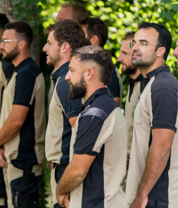 Un groupe d'employé Pottu & Seitz en uniforme beige et noir se tient debout à l'extérieur, entouré de verdure.