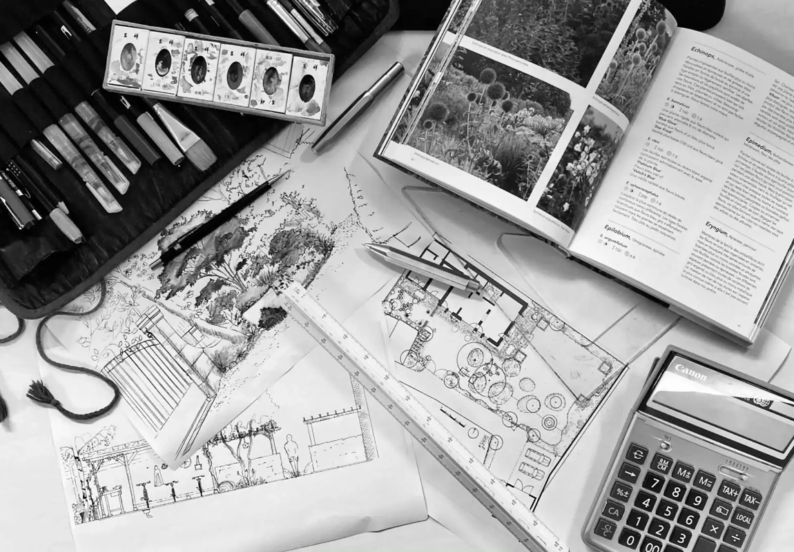 Matériel de dessin, livre ouvert, calculatrice, et plans architecturaux étalés sur une surface.